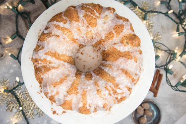 Eggnog bundt cake with glaze on a cake stand with Christmas lights around cake