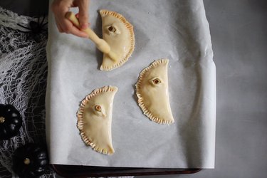 Brushing creepy eye calzones with egg wash